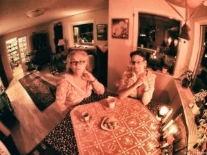 Two women at a table, dressed in onesies. The light is very pinkish red.
