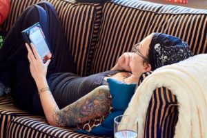 Courtnee lying down on a sofa, reading from her kindle. Her right arm is vividly tattooed.